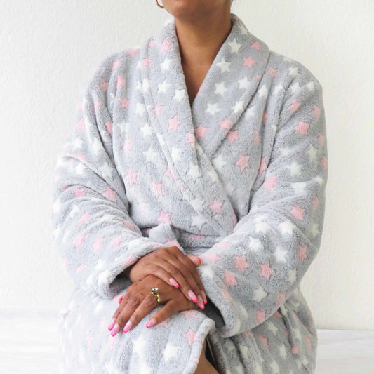 Grijze fleece badjas met roze en witte sterren, sjaalkraag, en handen met roze nagellak en ring in beeld
