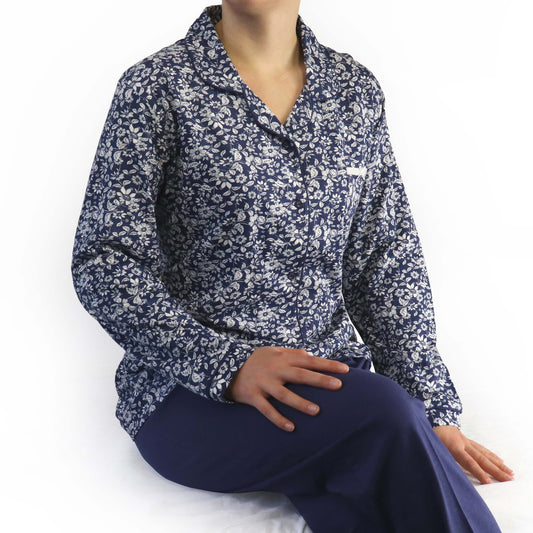 Blauwe dames pyjama met witte bloemenprint, lange mouwen en opstaande kraag, gedragen met blauwe broek.
