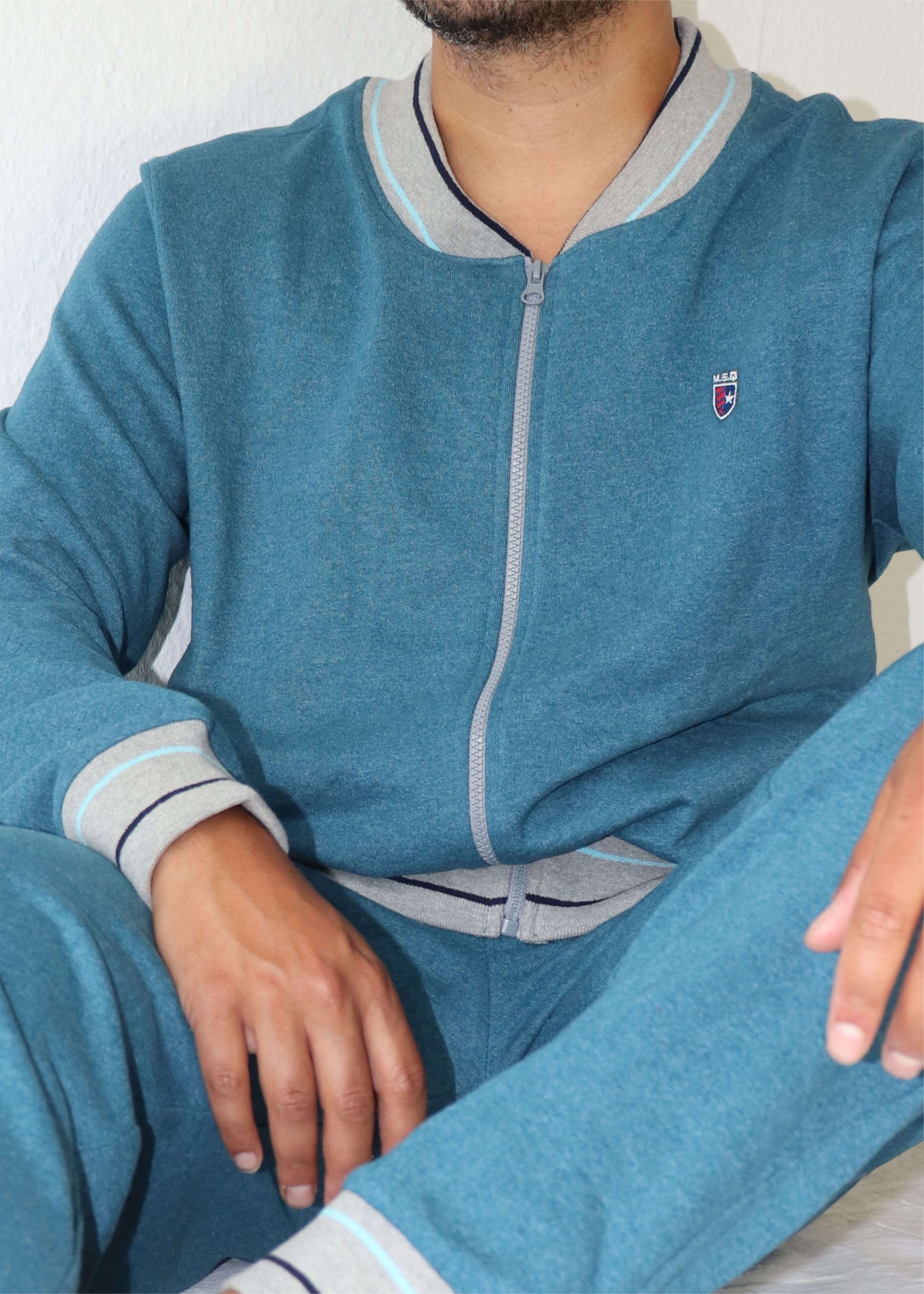 Blauw melange huispak met rits, grijze accenten op kraag en manchetten, en een klein logo op de borst.