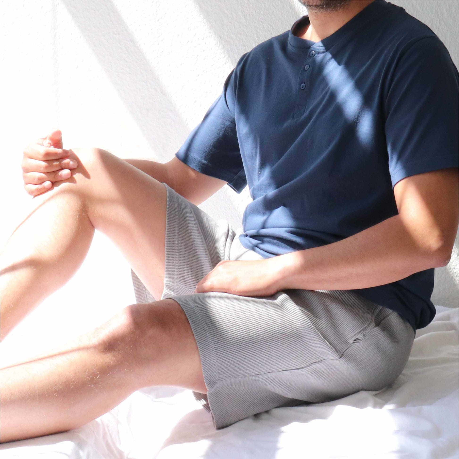 Man in blauwe shortama, zittend op wit oppervlak. Shirt met knoopsluiting, korte broek in wafelmotief.