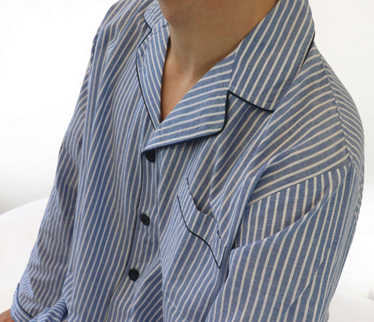 Close-up van een lichtblauwe gestreepte pyjama met doorknoop-stijl, toont kraag en borstzak detail.