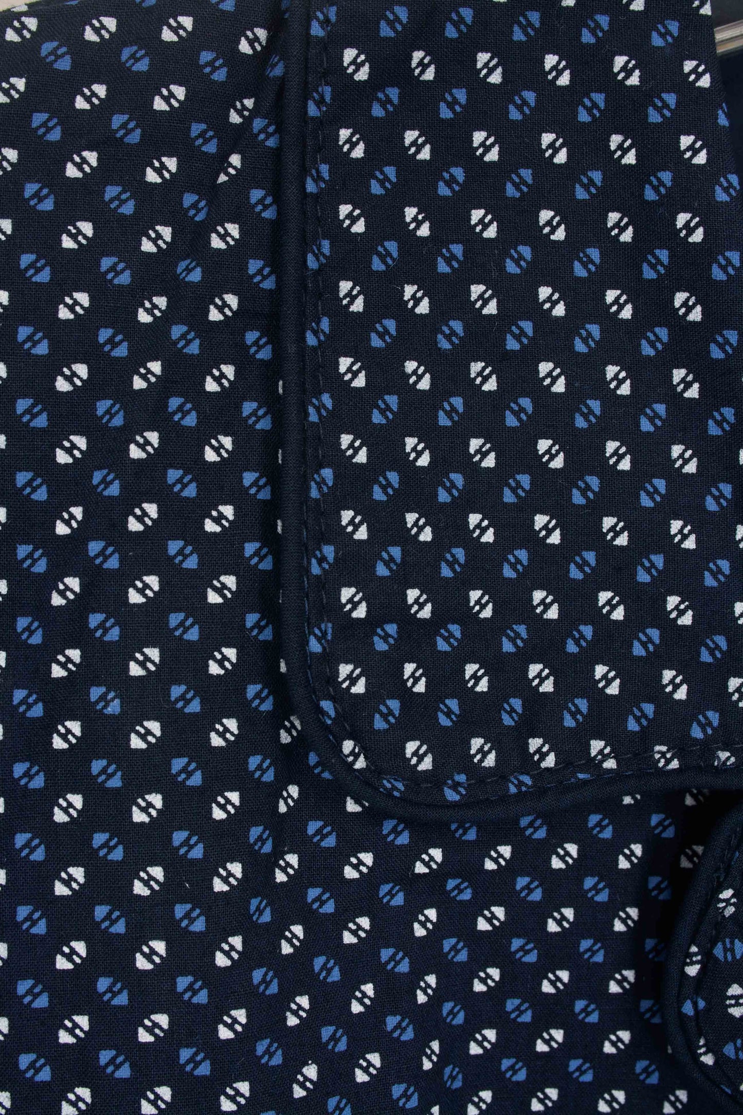 Close-up van donkerblauwe pyjamastof met wit en lichtblauw geometrisch patroon, zichtbare knoopsluiting.