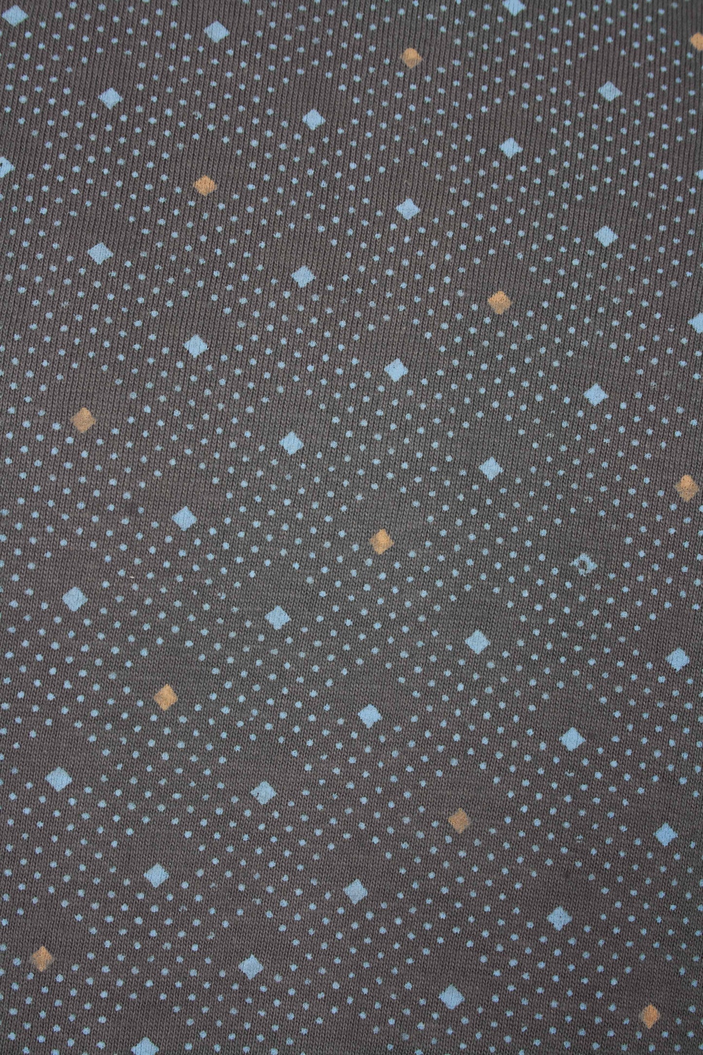 Grijze stof met lichtblauwe stippen en vierkantjes, en enkele oranje vierkantjes in een verspreid patroon.