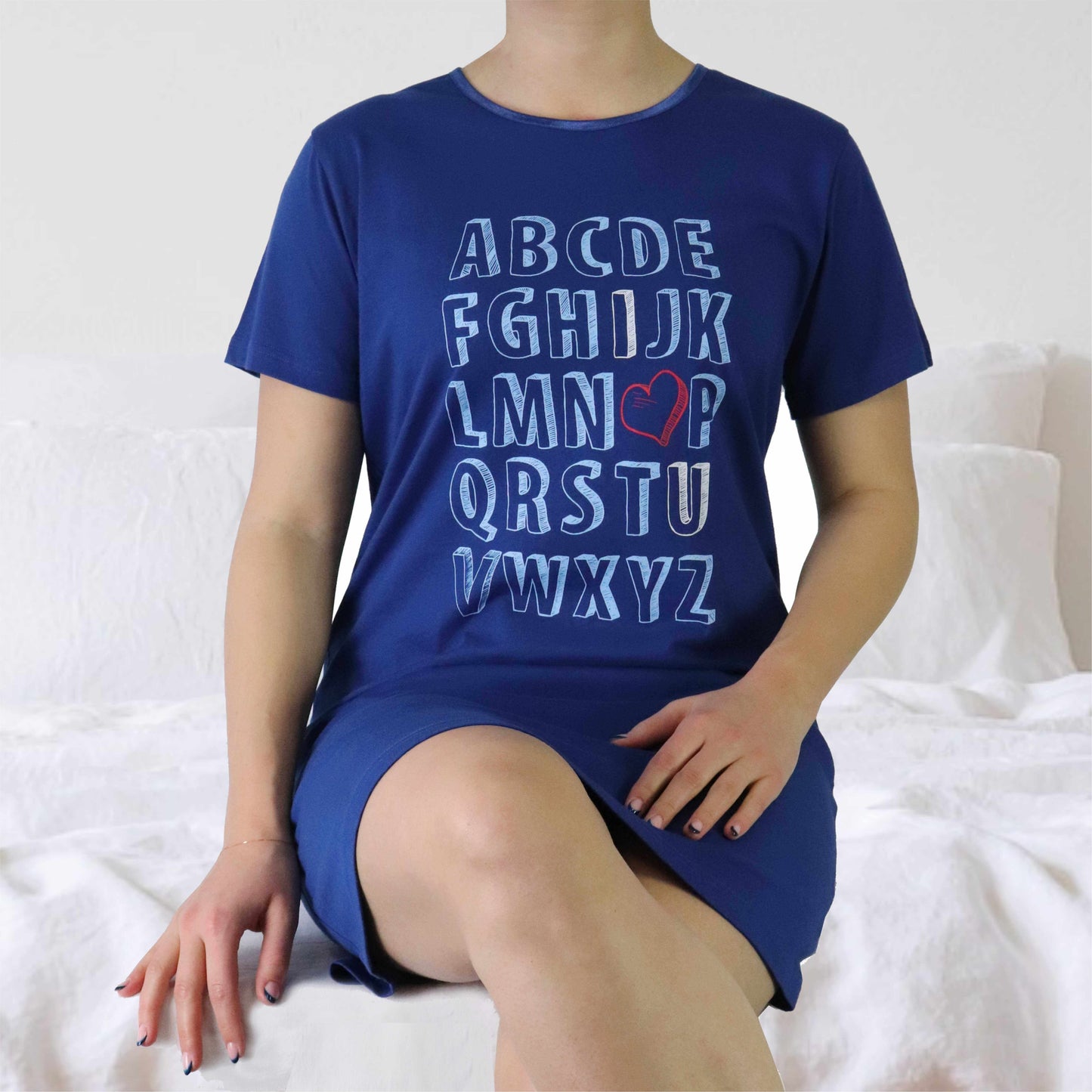 Marineblauw oversized damesshirt met alfabet print en rood hartje, gedragen door model op wit bed