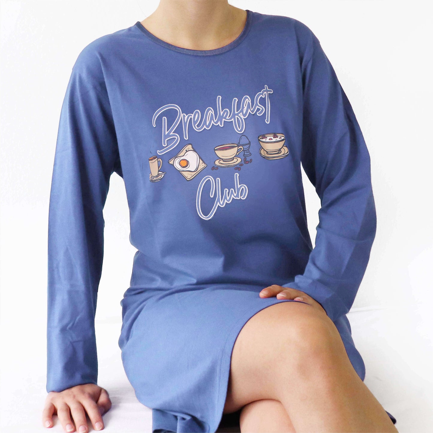 Blauw nachthemd met lange mouwen en 'Breakfast Club' opdruk, getoond op een persoon zittend op wit oppervlak