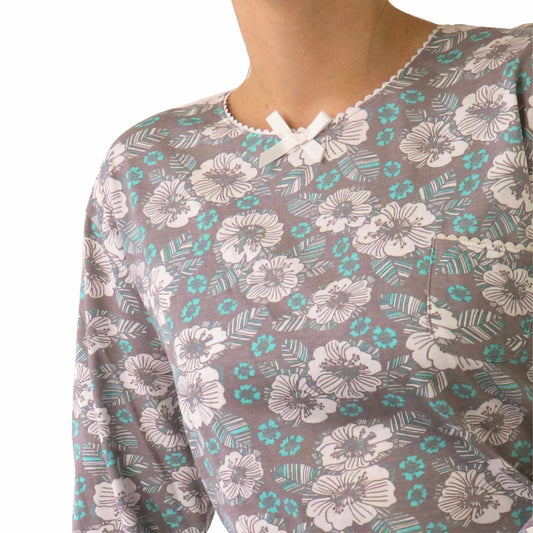 Close-up van een bruine pyjama met witte en turquoise bloemenprint, gemaakt van katoen met een kleine strik bij de hals.