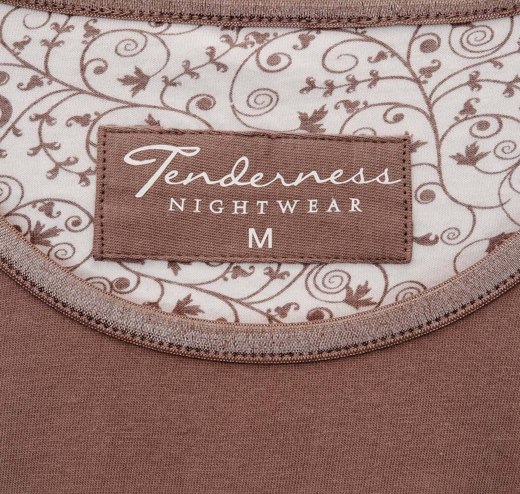 Close-up van een bruine Tenderness pyjama label op een wit kledingstuk met bruin bloemenpatroon.