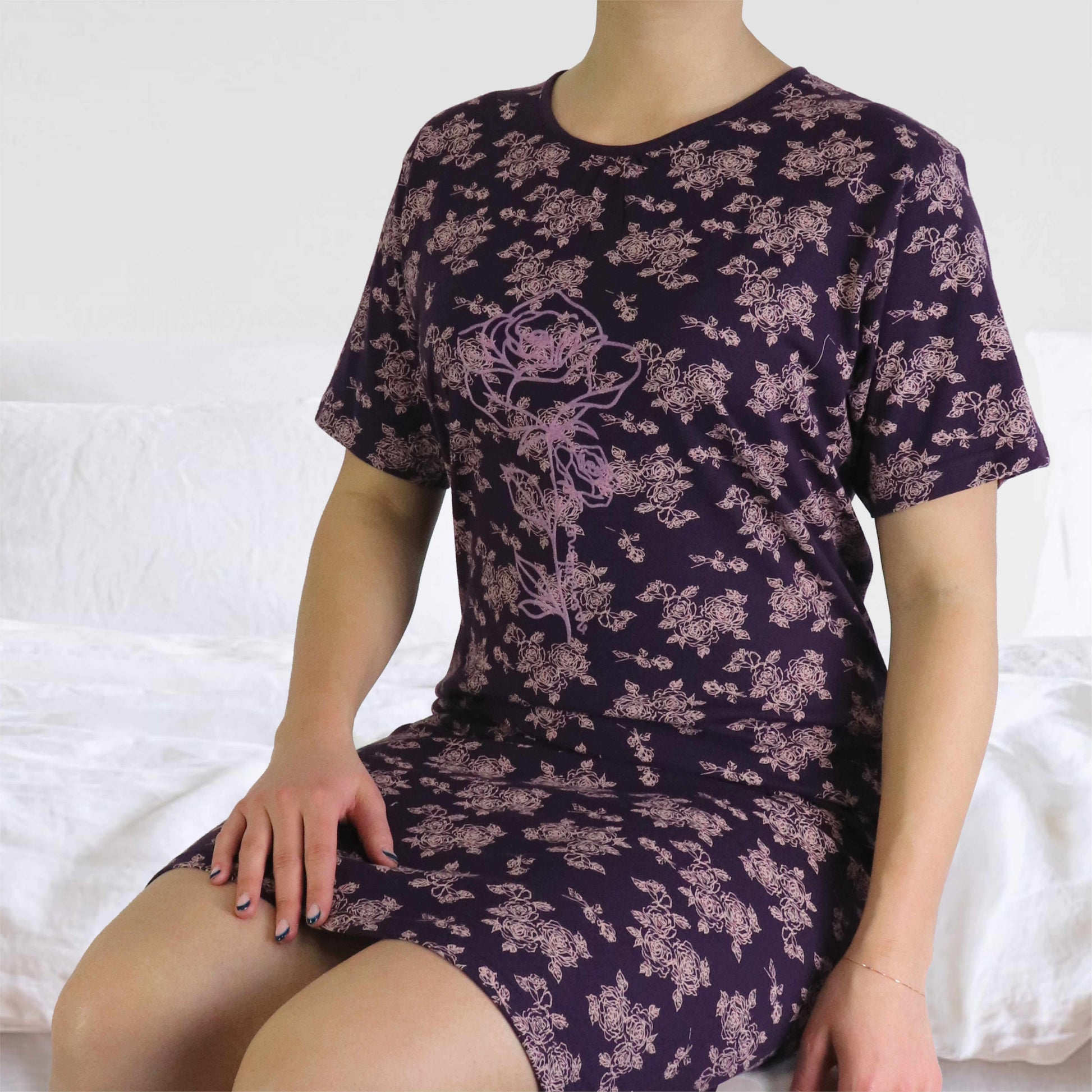 Lila nachthemd met roze bloemenprint, korte mouwen en ronde hals, gedragen door een model op een wit bed