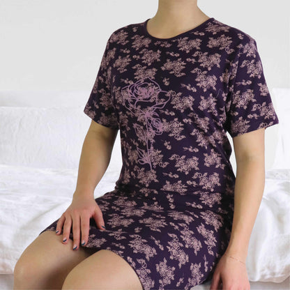 Lila nachthemd met roze bloemenprint, korte mouwen en ronde hals, gedragen door een model op een wit bed
