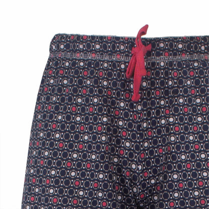 Close-up van pyjama broek met een geometrisch patroon van cirkels in donkerblauw, rood en wit, met een rood koordje.