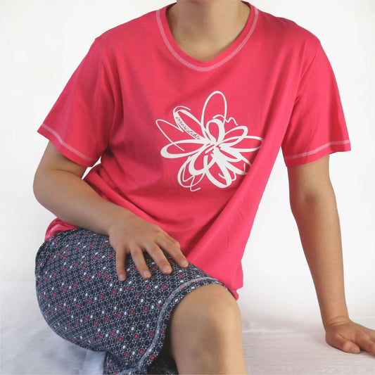 Rode dames pyjama met korte mouwen en witte bloem print, gedragen met een donkere broek met stippenpatroon.