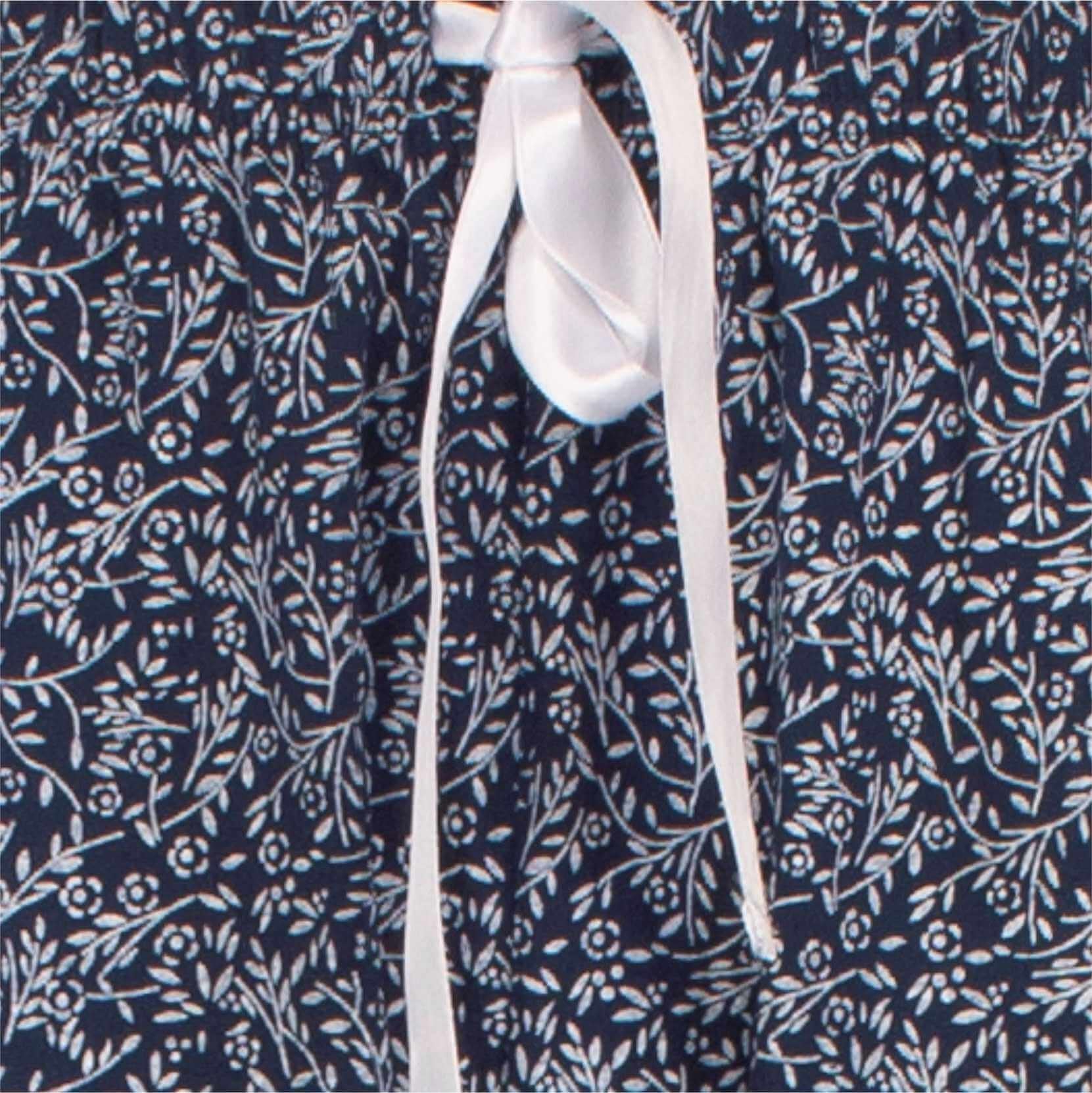 Witte strik op navy blauwe stof met delicaat bloemenpatroon, detail van een dames pyjama