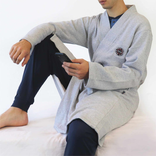 Man in grijze kimono-stijl badjas van sweatstof, zittend met gekruiste benen en een tablet vasthoudend.
