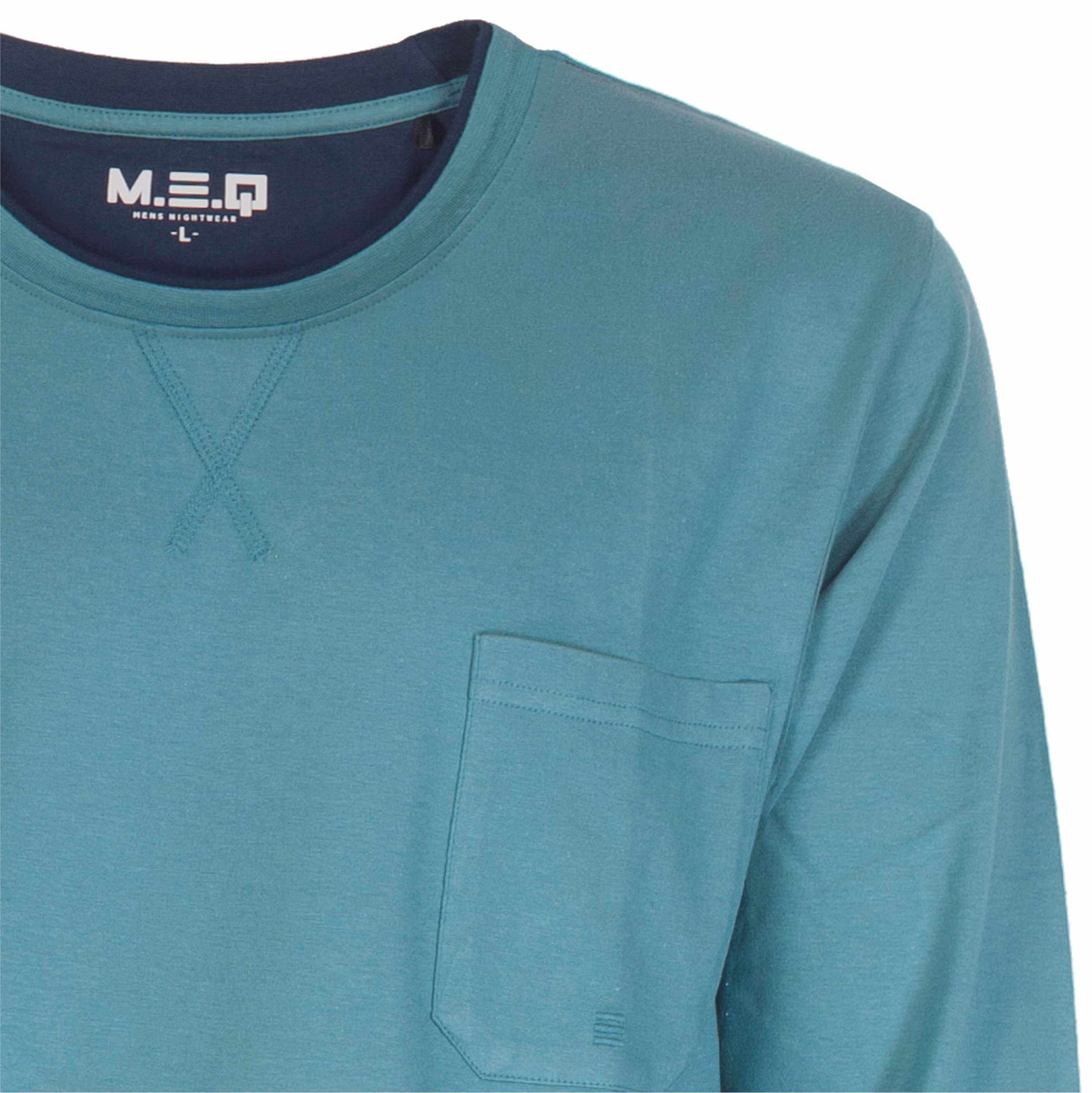 Close-up van een petrolblauwe pyjama top met lange mouwen, ronde hals en borstzakje. MEQ logo zichtbaar op de binnenkant.