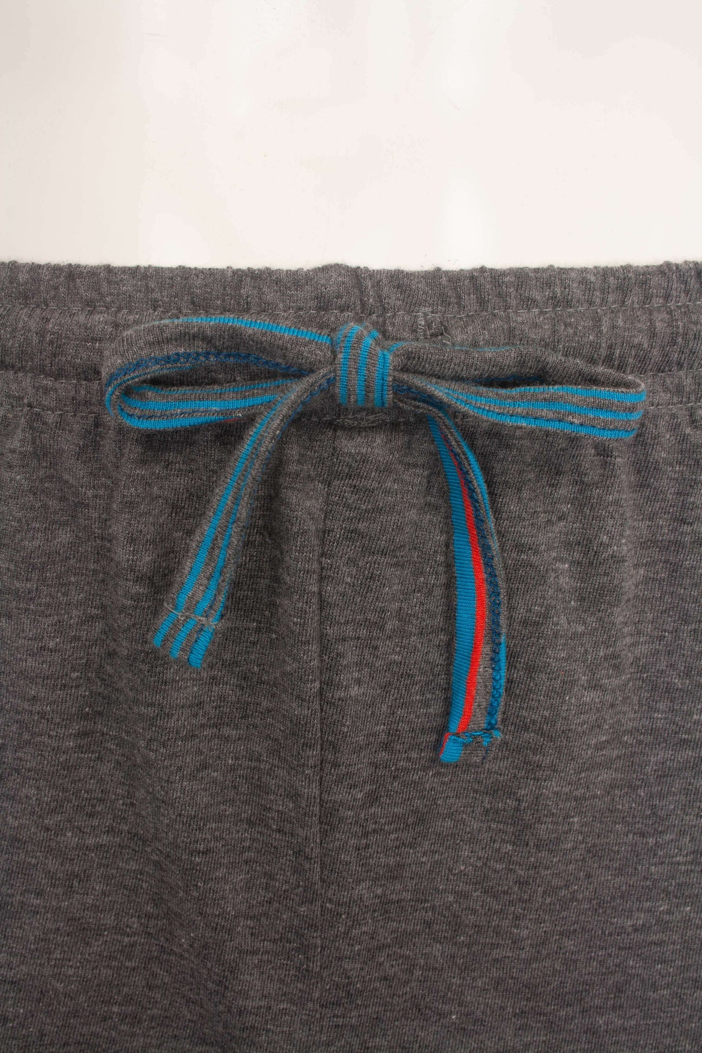 Grijze pyjama broek met een blauw en rood gestreept trekkoord aan de taille, close-up van de tailleband.