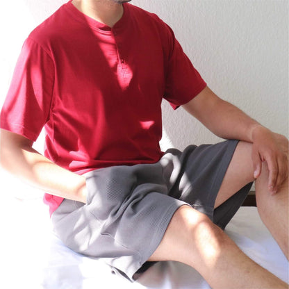 Man in rode shortama, bestaande uit T-shirt met knoopjes en grijze korte broek, zittend op witte ondergrond