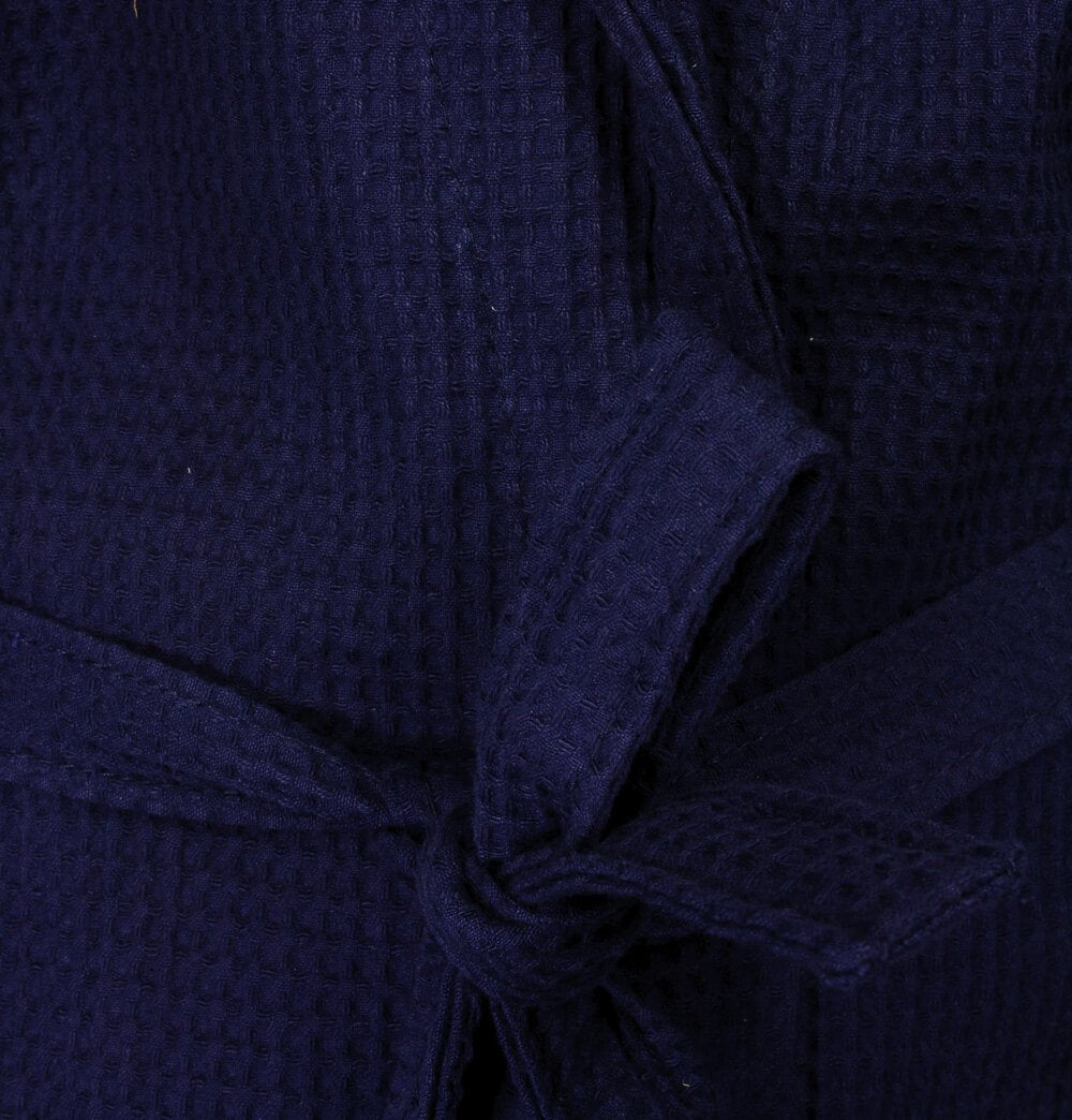 Close-up van donkerblauwe wafeltextuur stof, vermoedelijk van een badjas, met een gevouwen detail zichtbaar.
