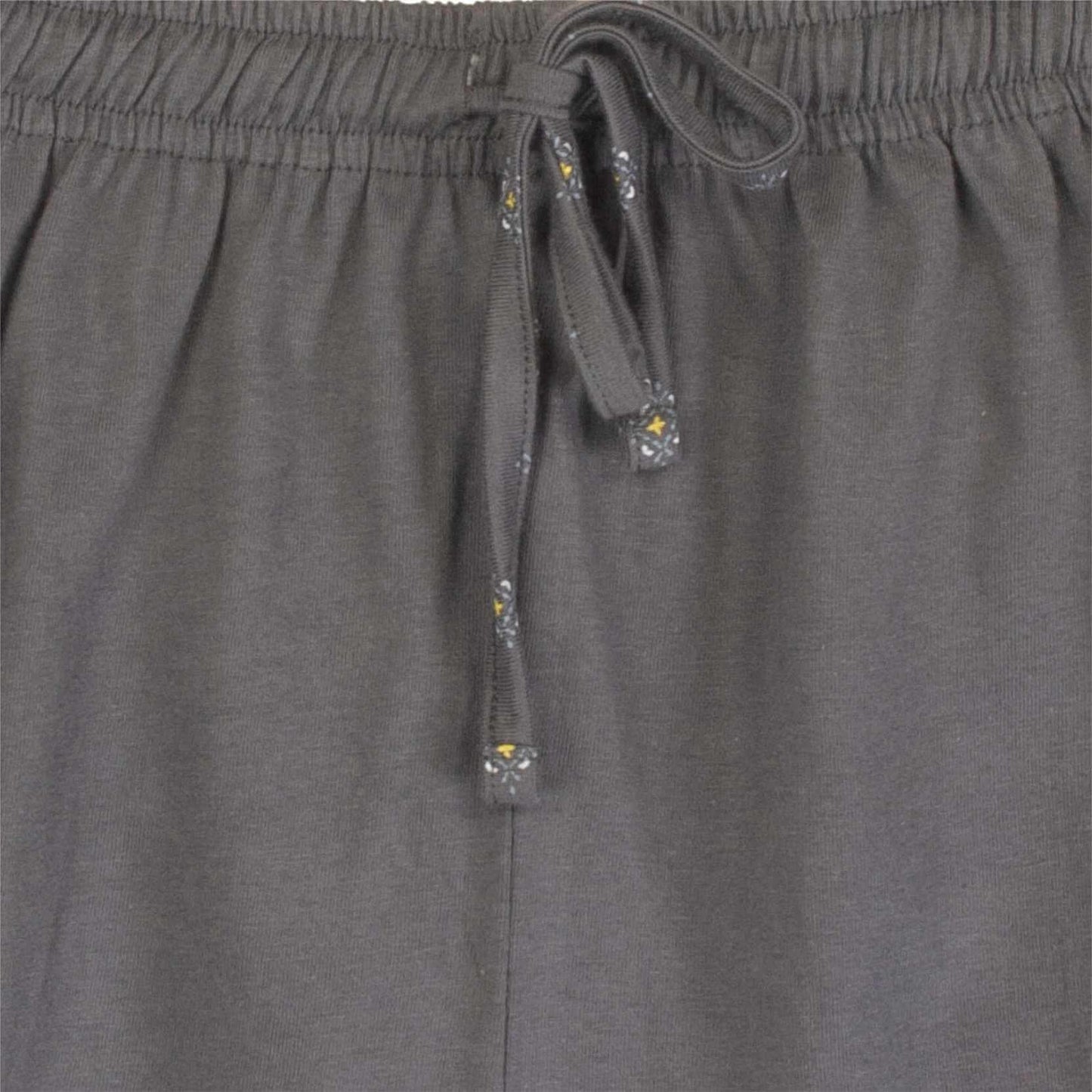 Close-up van de taille van een grijze pyjama broek met een elastische band en een koord met decoratieve uiteinden.