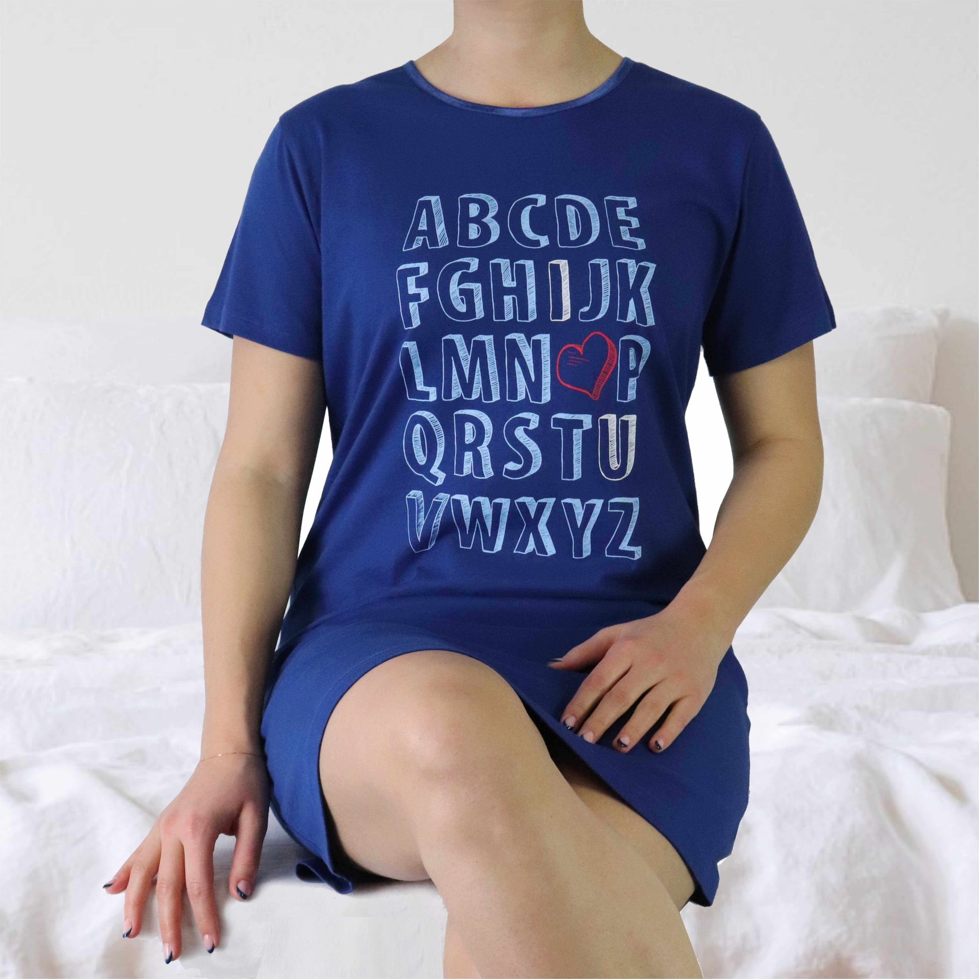 Marineblauw oversized damesshirt met alfabet print en rood hartje, gedragen door model op wit bed