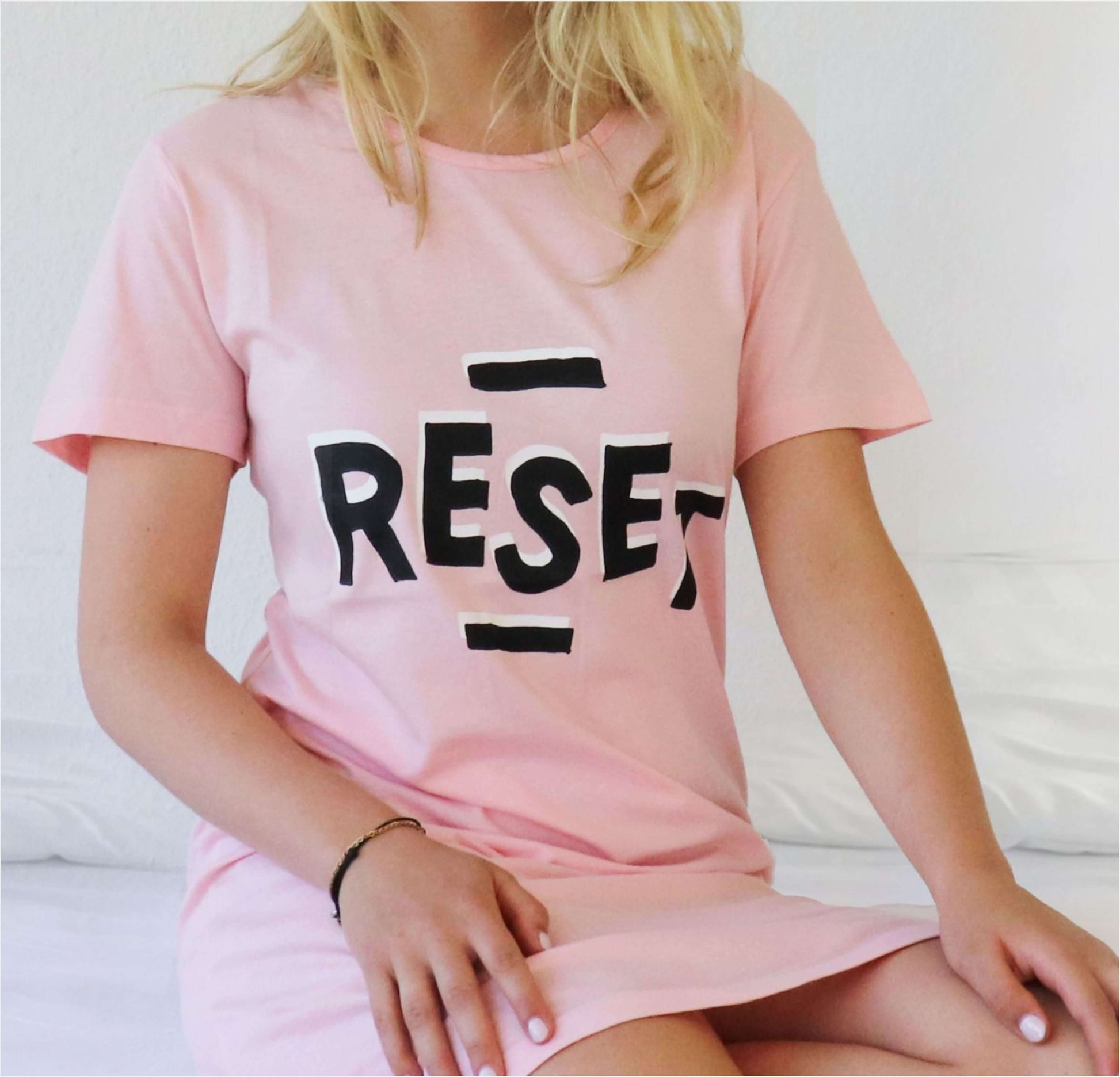Roze nachthemd met korte mouwen en 'RESET' tekst in zwarte letters op de vogedragen door een blonde vrouw