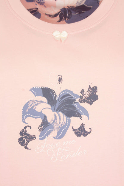 Roze nachthemd met ronde hals, versierd met een blauwe bloem en een kleine witte strik op de borst.