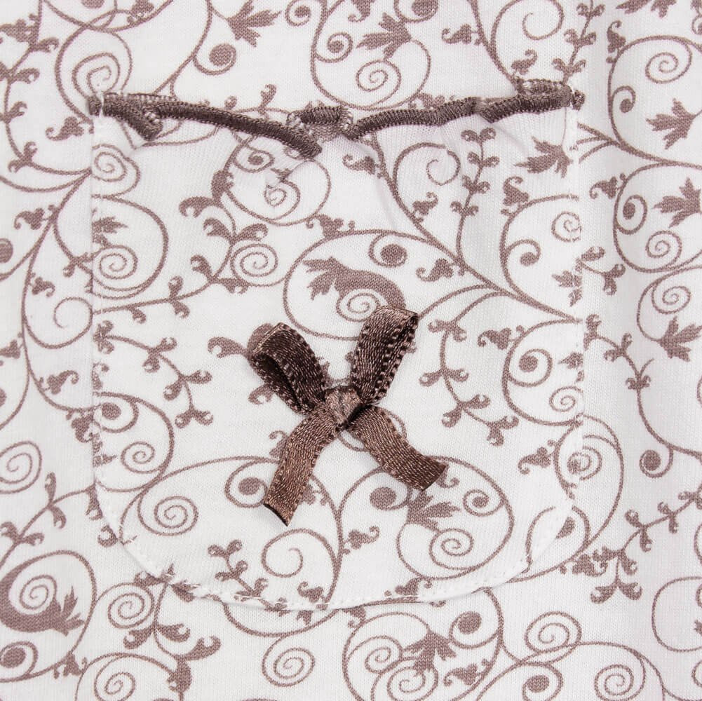 Bruine bloemenprint op witte stof van dames pyjama, met satijnen strikje en aantrekkoord zichtbaar.