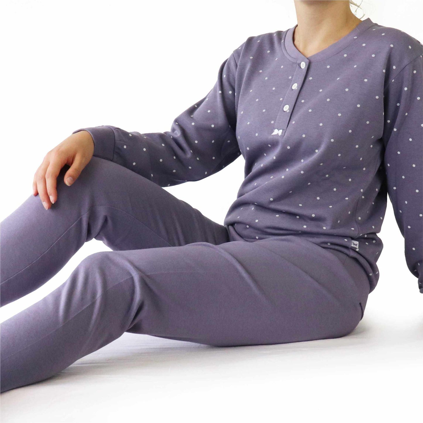 Lila fleece pyjama met witte stippen, lange mouwen en knopen aan de hals, gedragen door een zittend model.