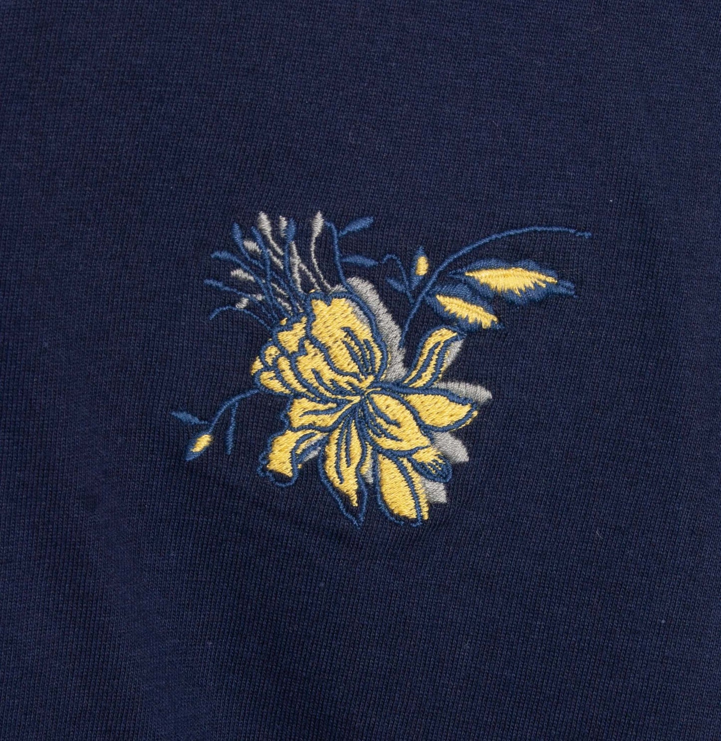 Donkerblauwe stof met geborduurde gele bloem, detail van een pyjama top