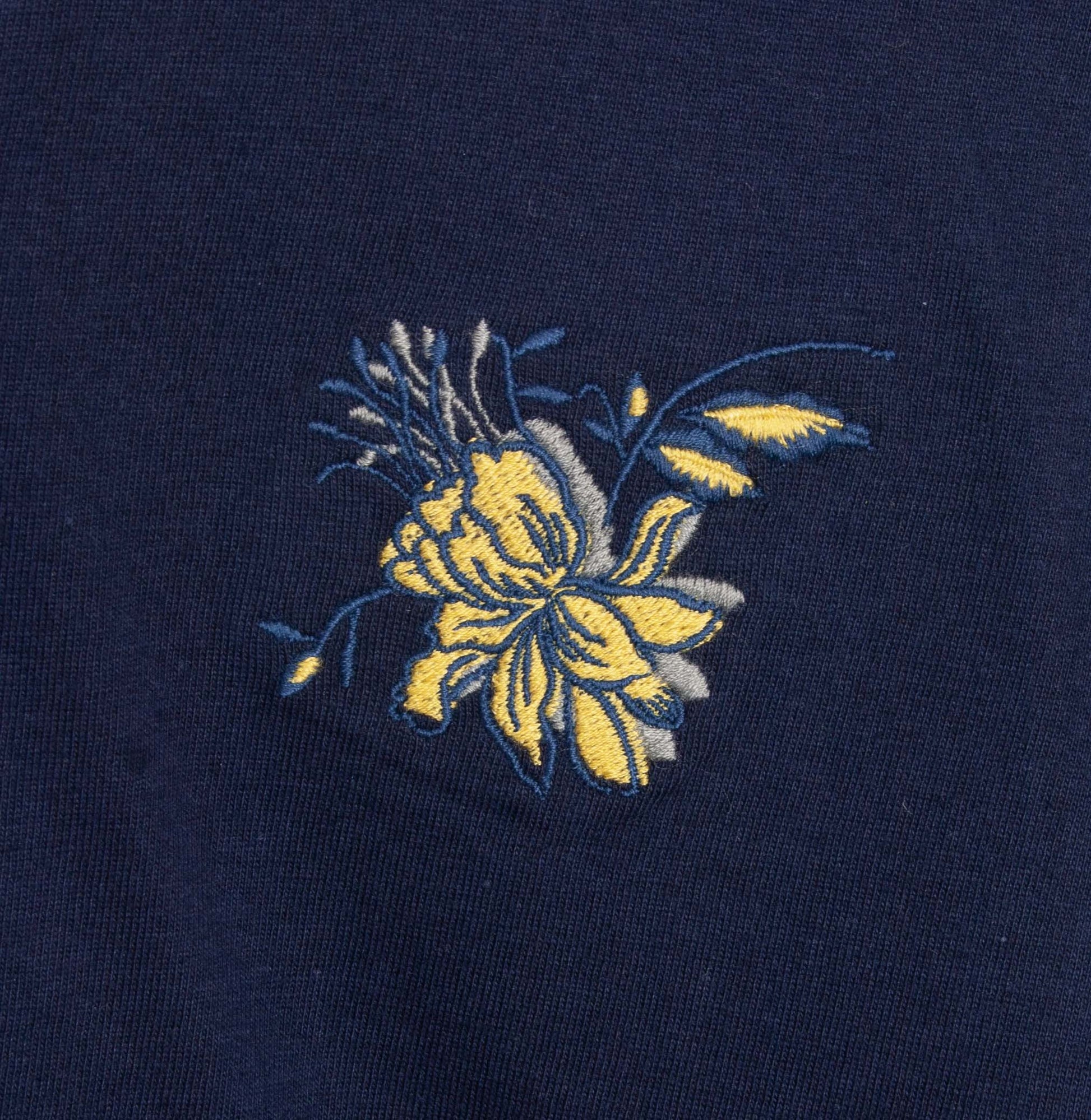Donkerblauwe stof met geborduurde gele bloem, detail van een pyjama top
