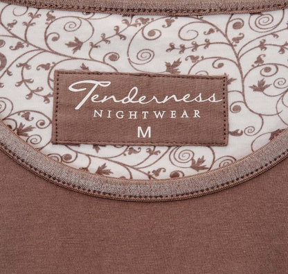 Close-up van een bruine Tenderness pyjama label op een wit kledingstuk met bruin bloemenpatroon.