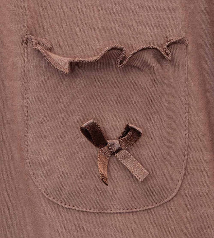 Close-up van bruin katoenen pyjama-topje met opgestikt borstzakje en satijnen strikje, gerafelde hals.