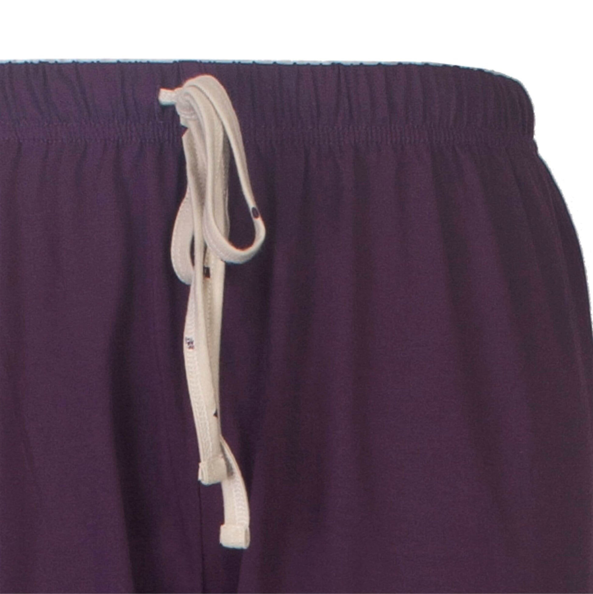 Close-up van een paarse pyjama broek met een beige koord om de taille vast te maken.