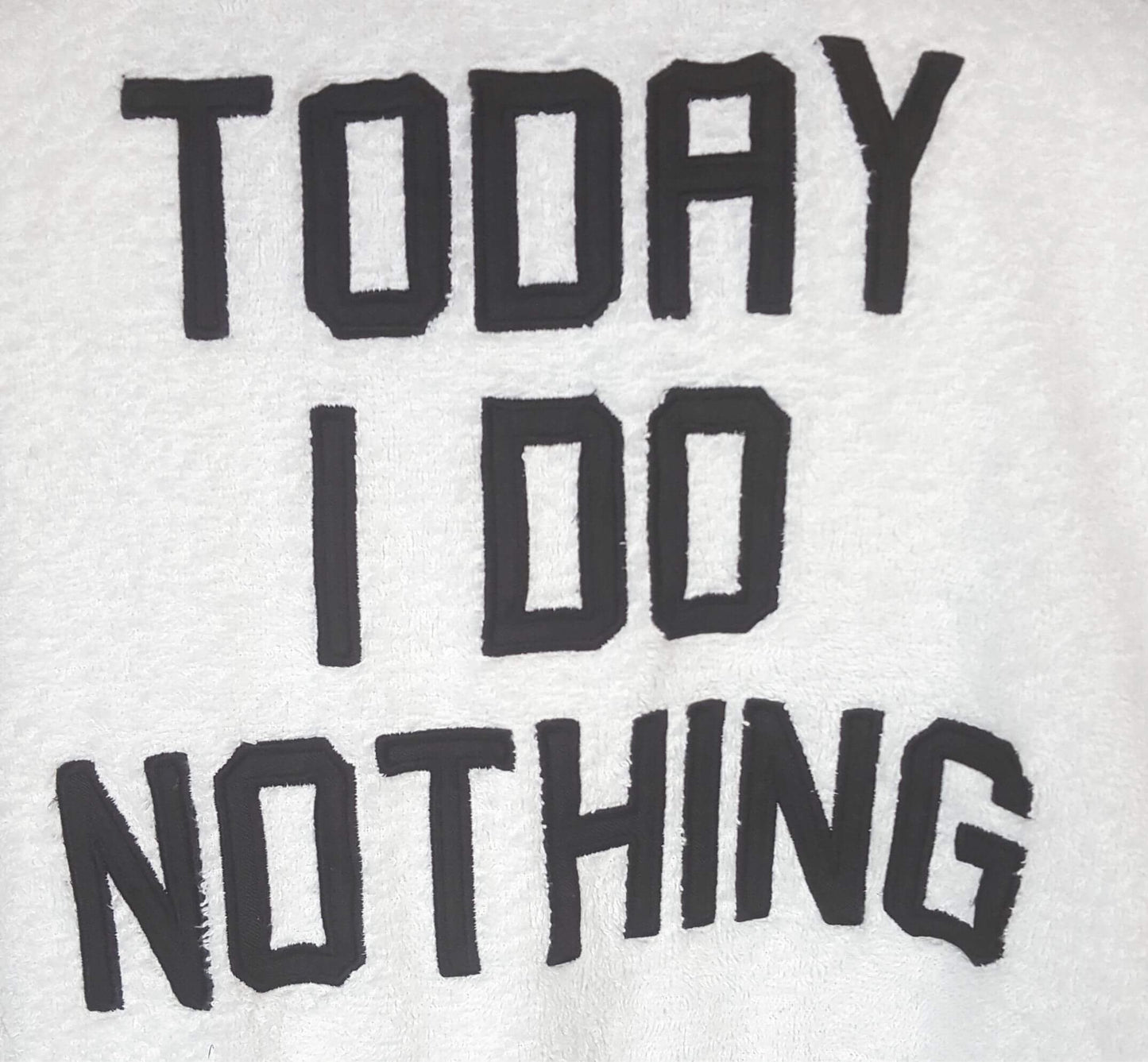 Zwarte tekst 'TODAY I DO NOTHING' op een witte achtergrond, mogelijk een badjas of kledingstuk.