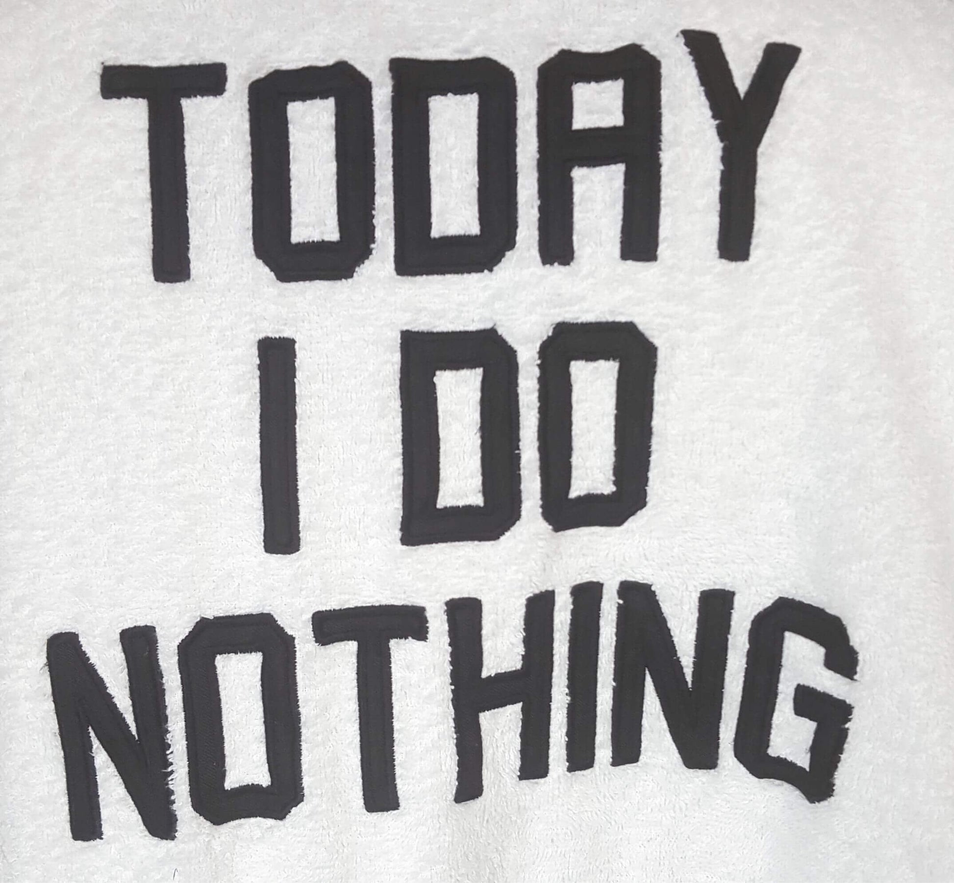 Zwarte tekst 'TODAY I DO NOTHING' op een witte achtergrond, mogelijk een badjas of kledingstuk.